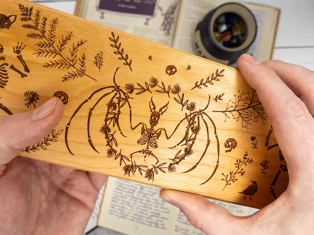 Wooden dice vault with engraved deer and floral design held by hands, for tabletop gaming