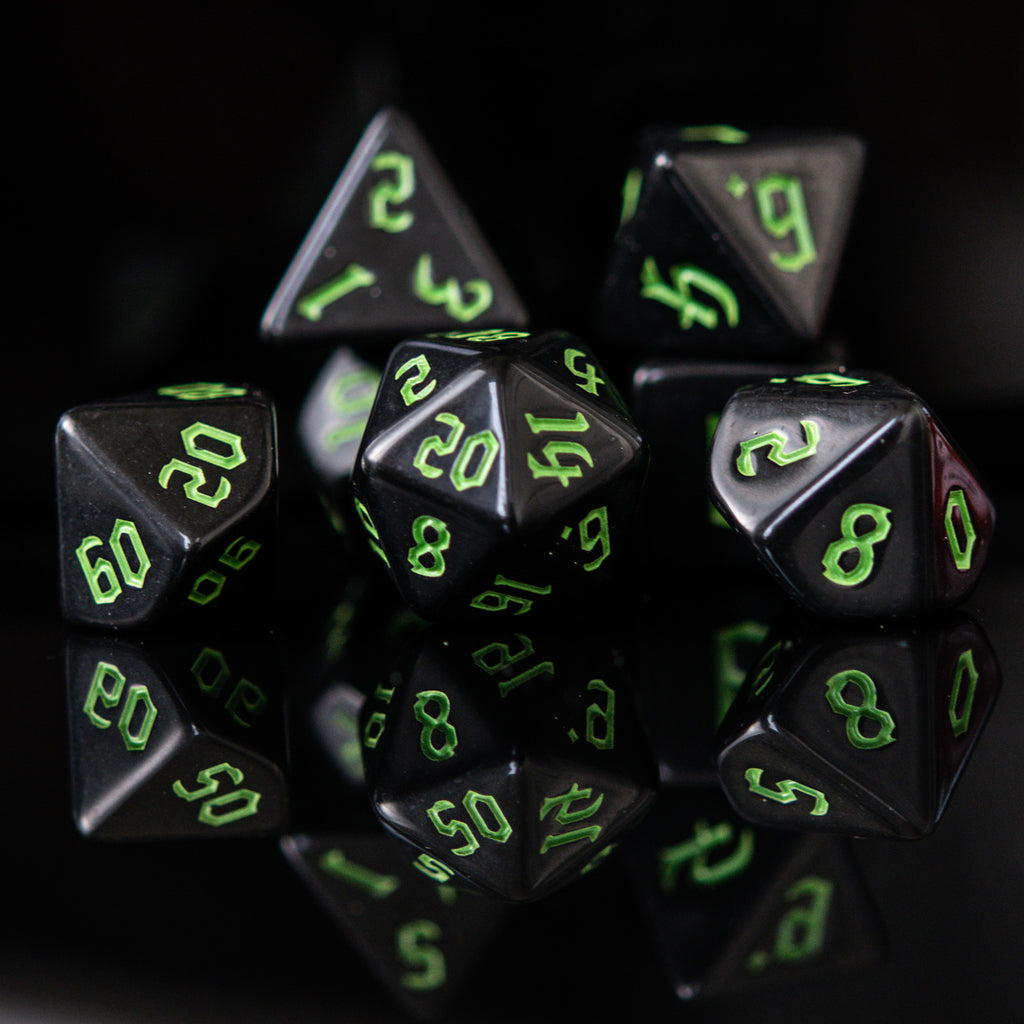 A set of black acrylic dice with green gothic style numbers, including various shapes typical for role-playing games.