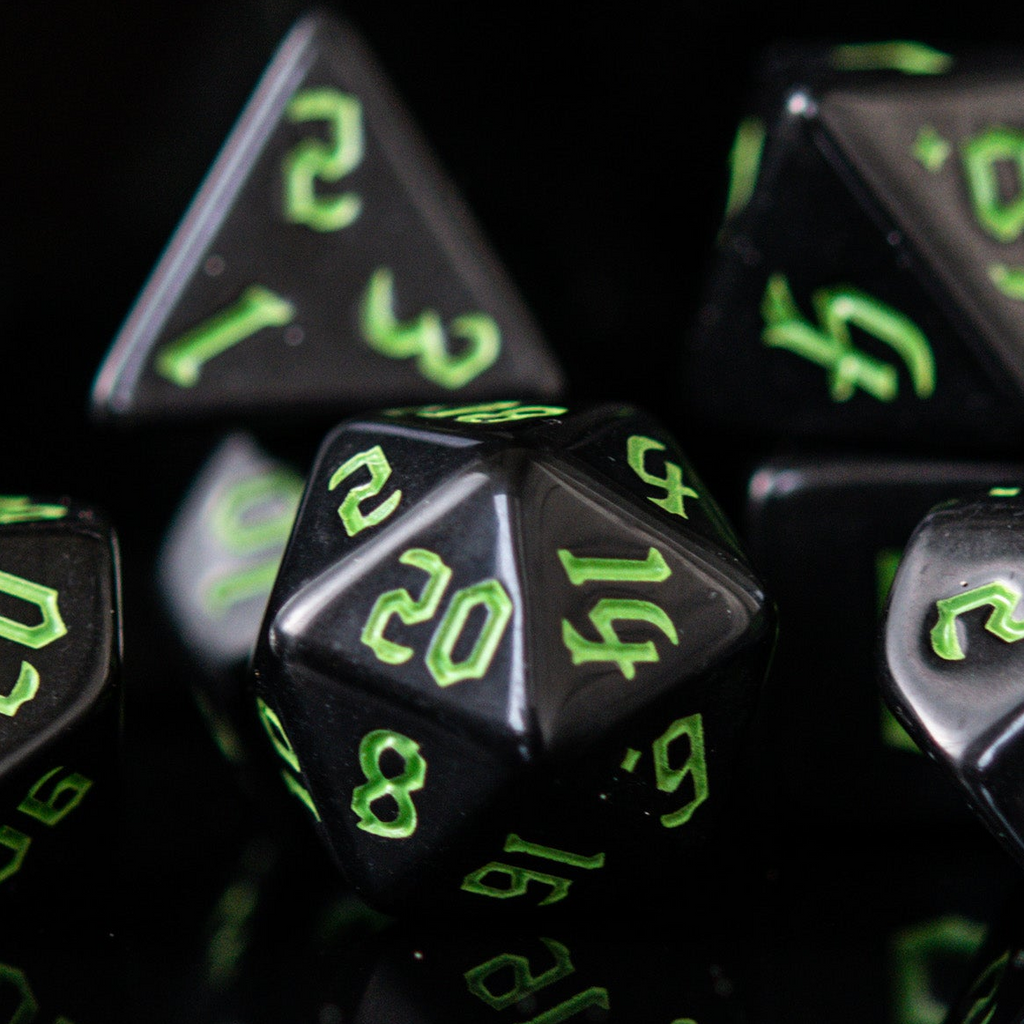 A set of black acrylic dice with green gothic style numbers, including various shapes typical for role-playing games.