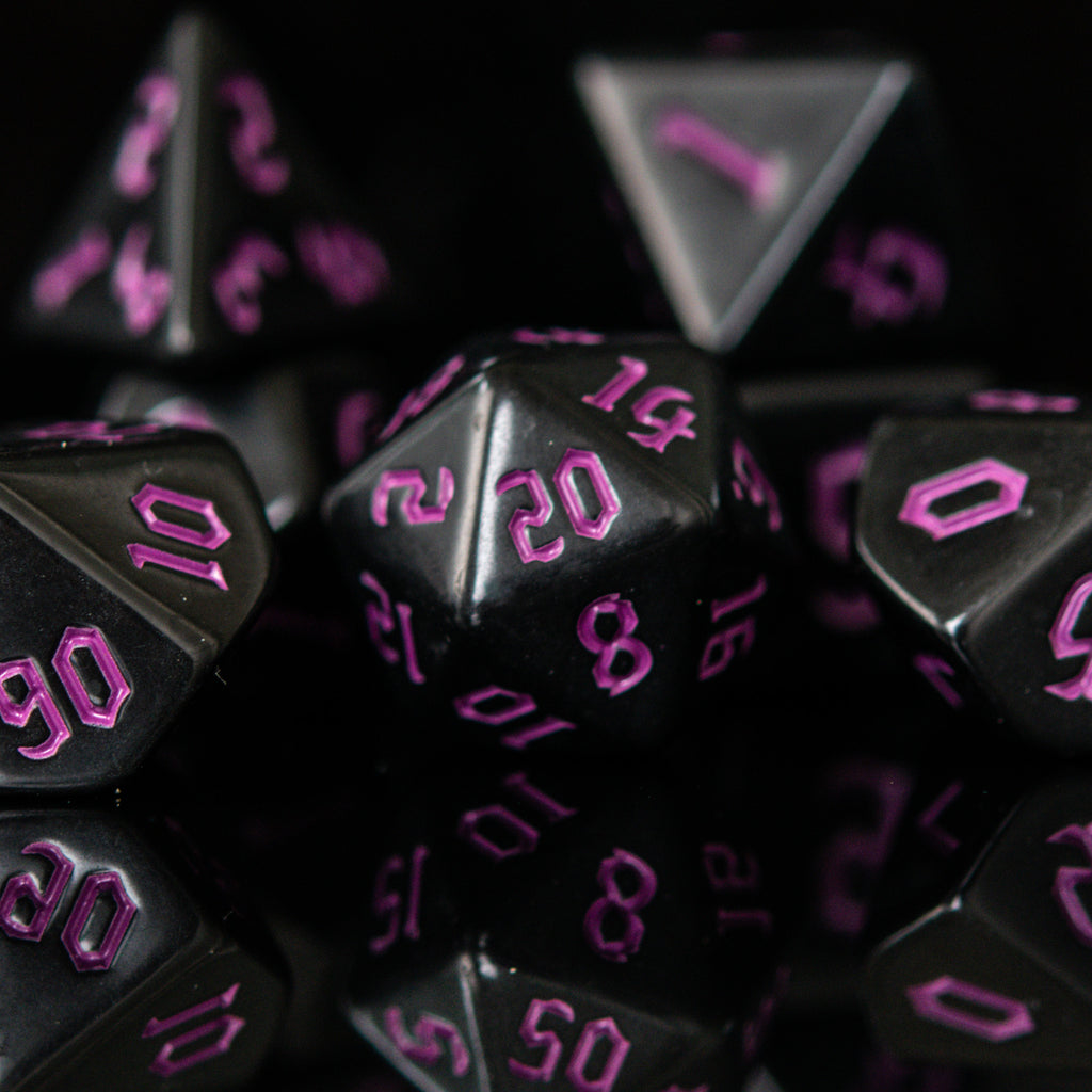 A set of black acrylic dice with engraved purple gothic font numbers, displayed on a reflective surface.