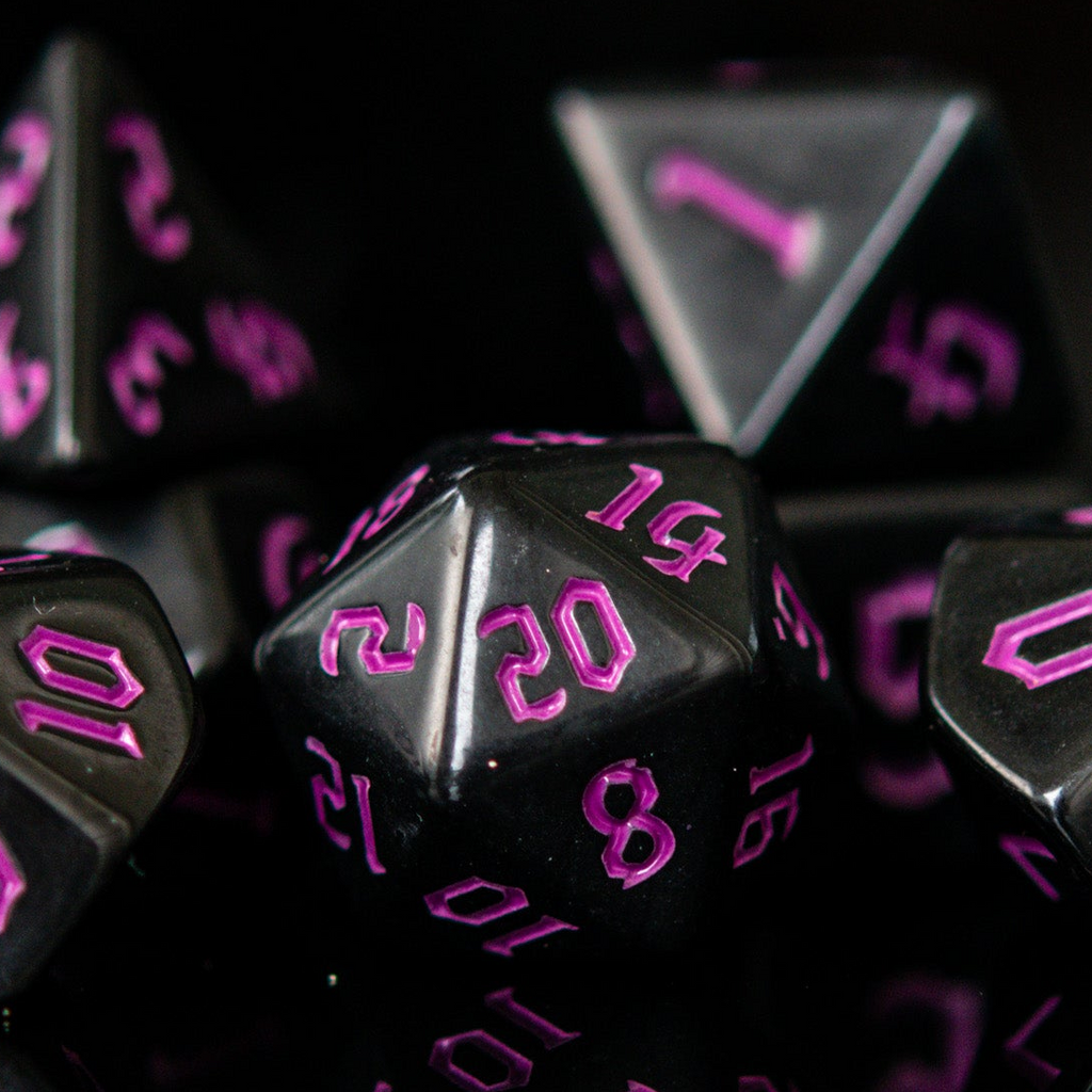 A set of black acrylic dice with engraved purple gothic font numbers, displayed on a reflective surface.