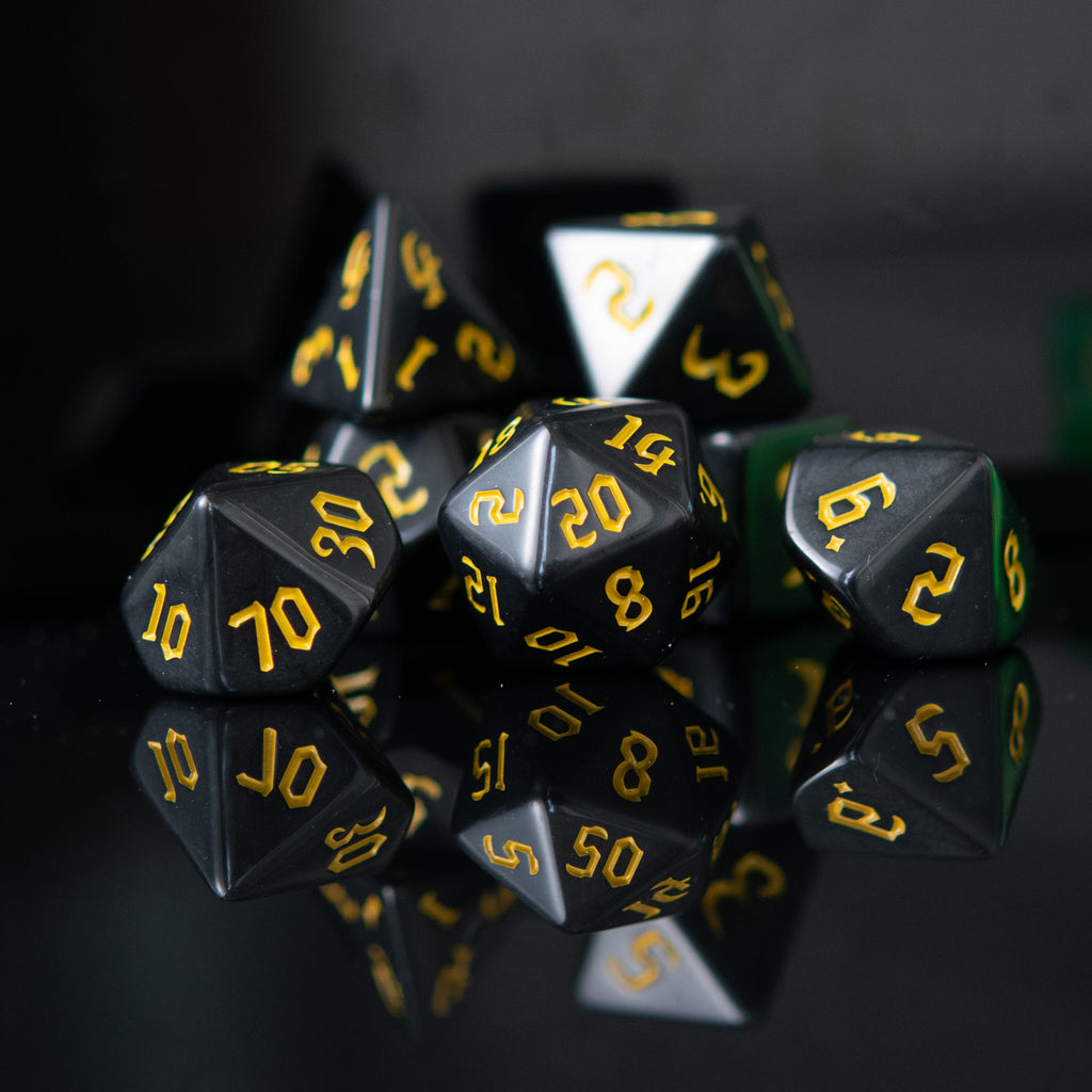 A set of black acrylic dice with yellow numbers, including various shapes typical for role-playing games.