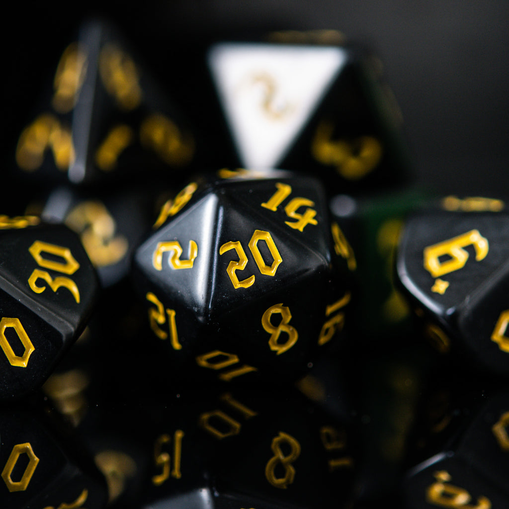 A set of black acrylic dice with yellow numbers, including various shapes typical for role-playing games.