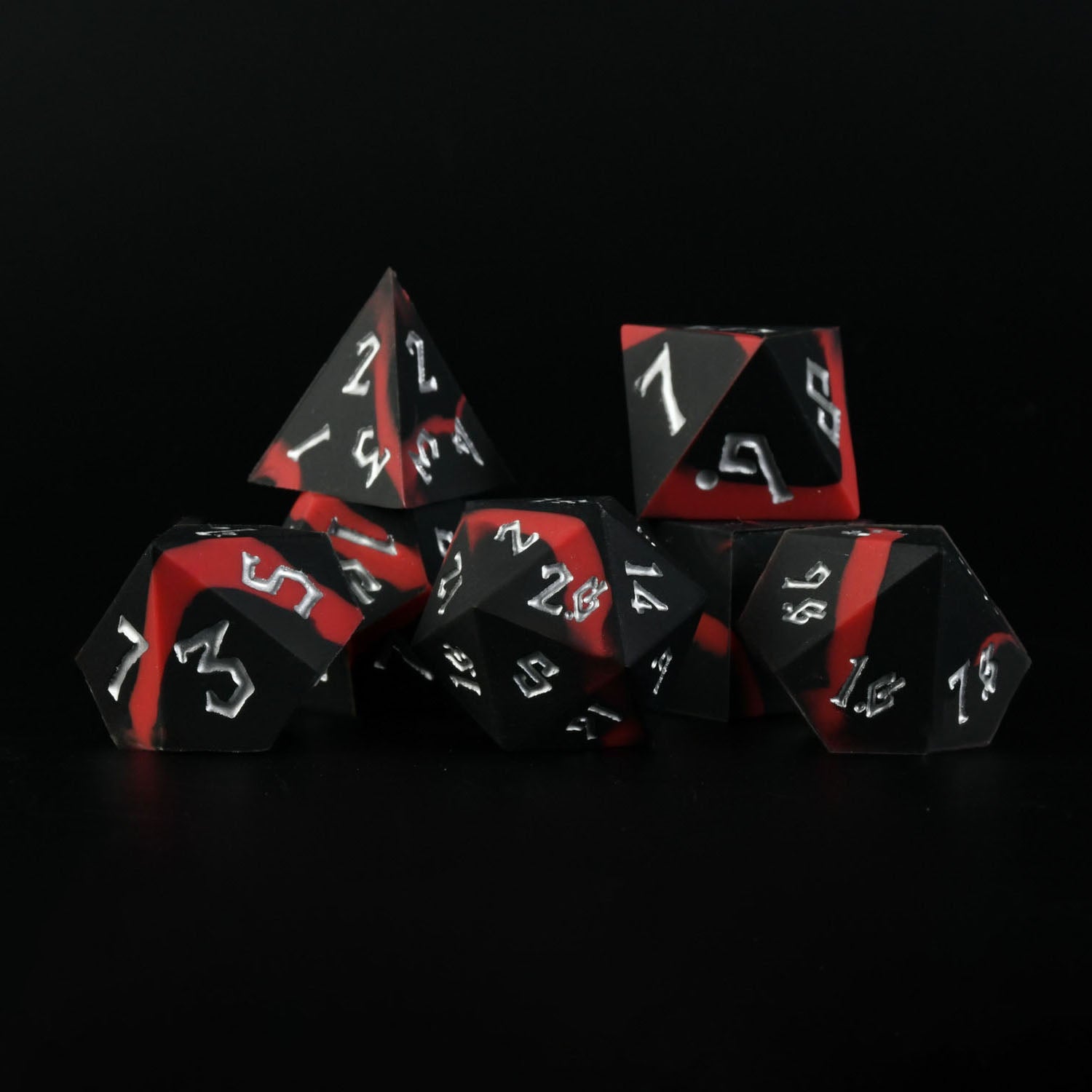 A set of silicone dice in black and red with white engravings, including various shapes such as a d4, d6, d8, d10, d12, and d20.