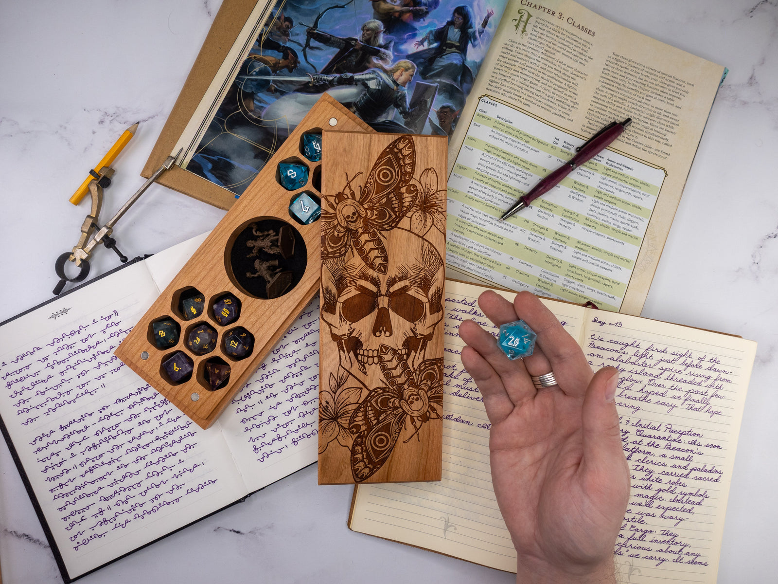 Wooden dice tray with engraved designs on a marble surface with notebooks and pens.