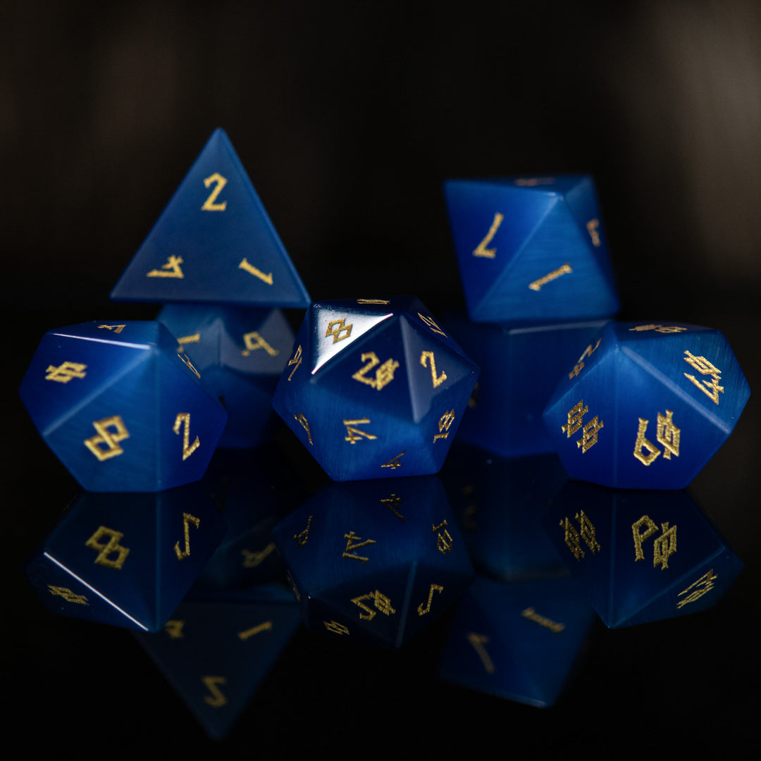 A set of blue gemstone dice with engraved numbers, reflecting on a dark surface.