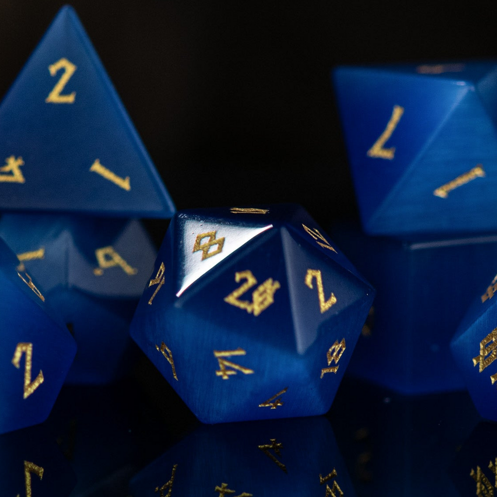 A set of blue gemstone dice with engraved numbers, reflecting on a dark surface.