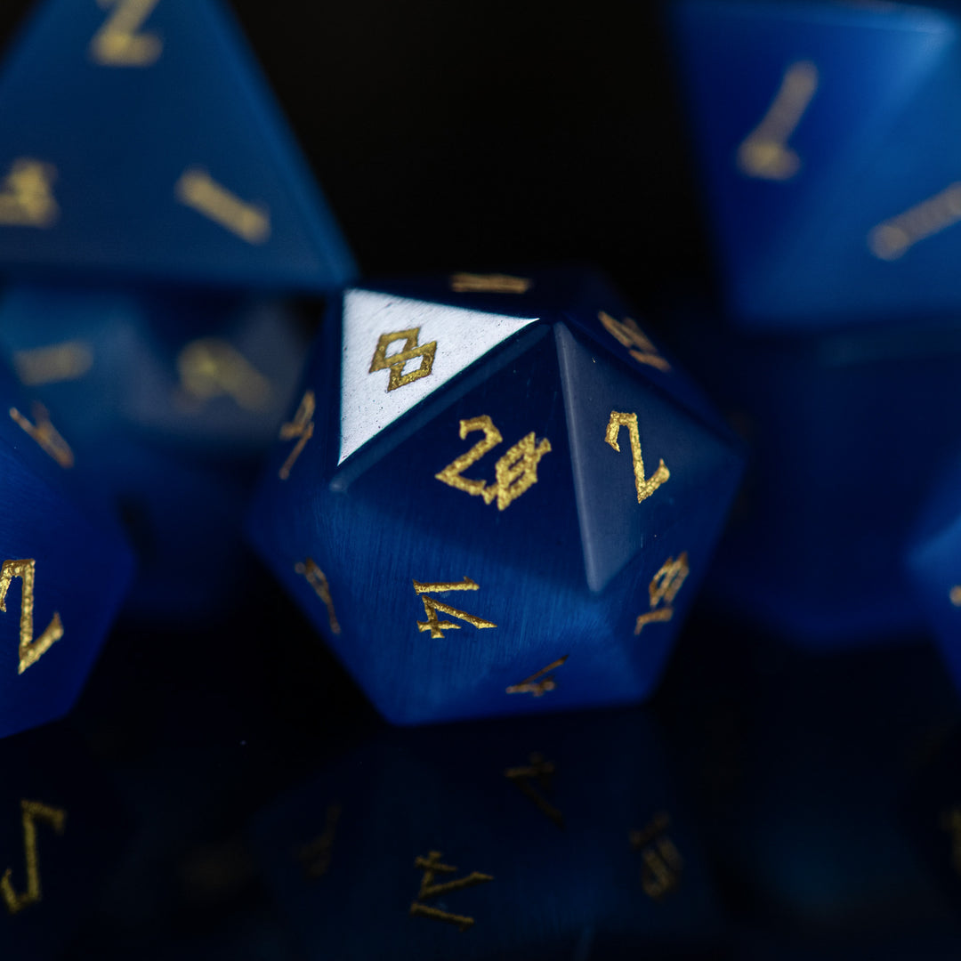A set of blue gemstone dice with engraved numbers, reflecting on a dark surface.