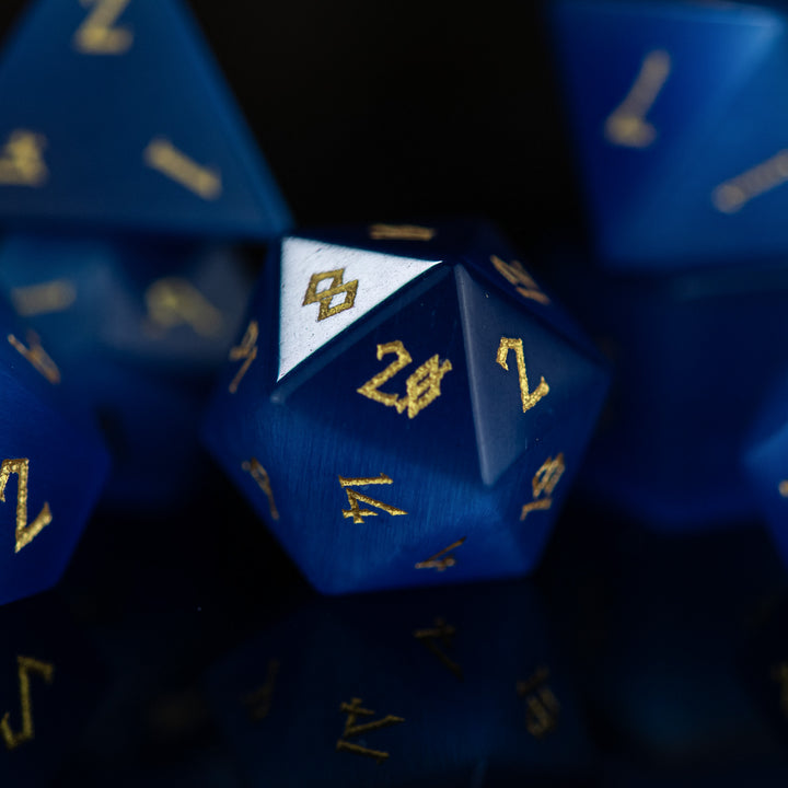 A set of blue gemstone dice with engraved numbers, reflecting on a dark surface.