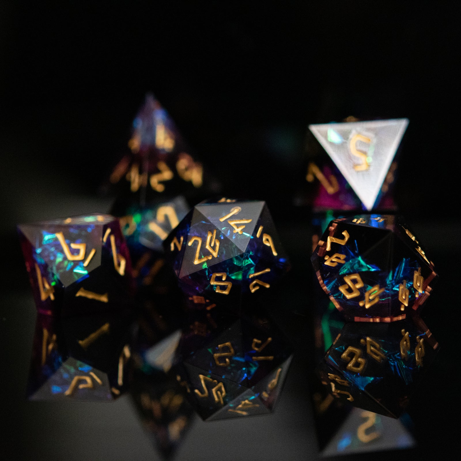 a set of dark sharp edge resin polyhedral dnd dice with iridescent foil inside and gold numbering. 