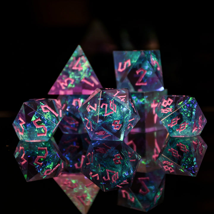A set of sharp-edged, multicolored resin dnd dice with pink hand-painted numbers, reflecting a vibrant blue, green and purple glow.