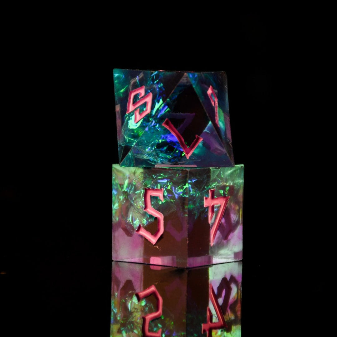 A set of sharp-edged, multicolored resin dnd dice with pink hand-painted numbers, reflecting a vibrant blue, green and purple glow.