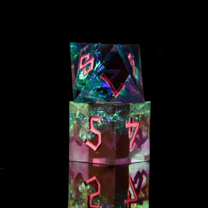 A set of sharp-edged, multicolored resin dnd dice with pink hand-painted numbers, reflecting a vibrant blue, green and purple glow.