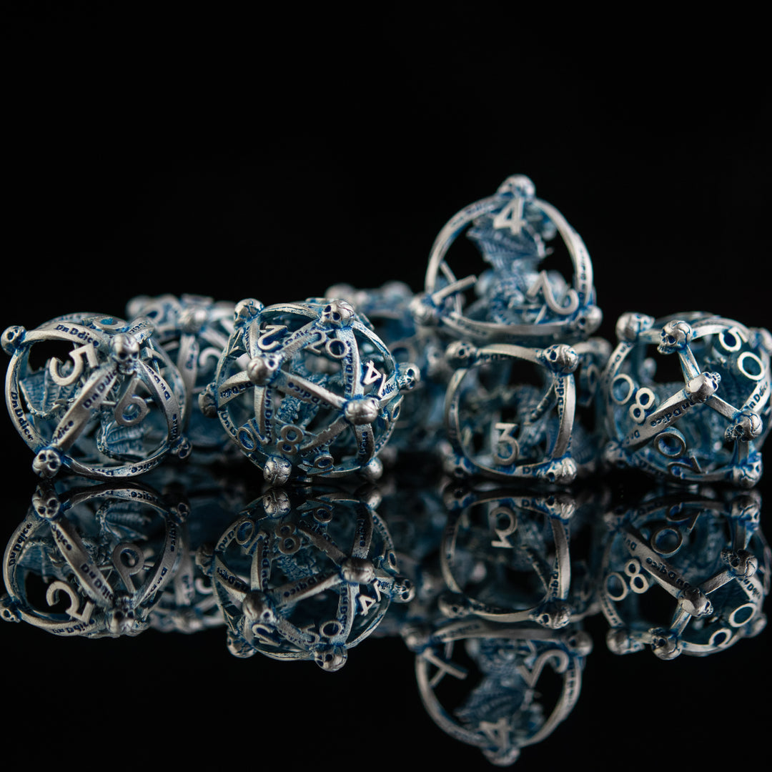 A set of hollow metal dice in silver and blue, displayed on a reflective surface.