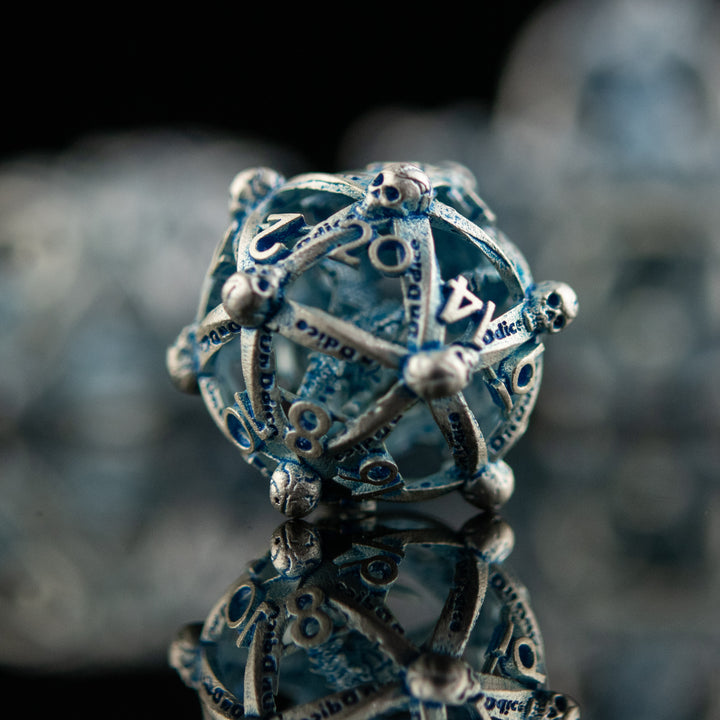 A set of hollow metal dice in silver and blue, displayed on a reflective surface.
