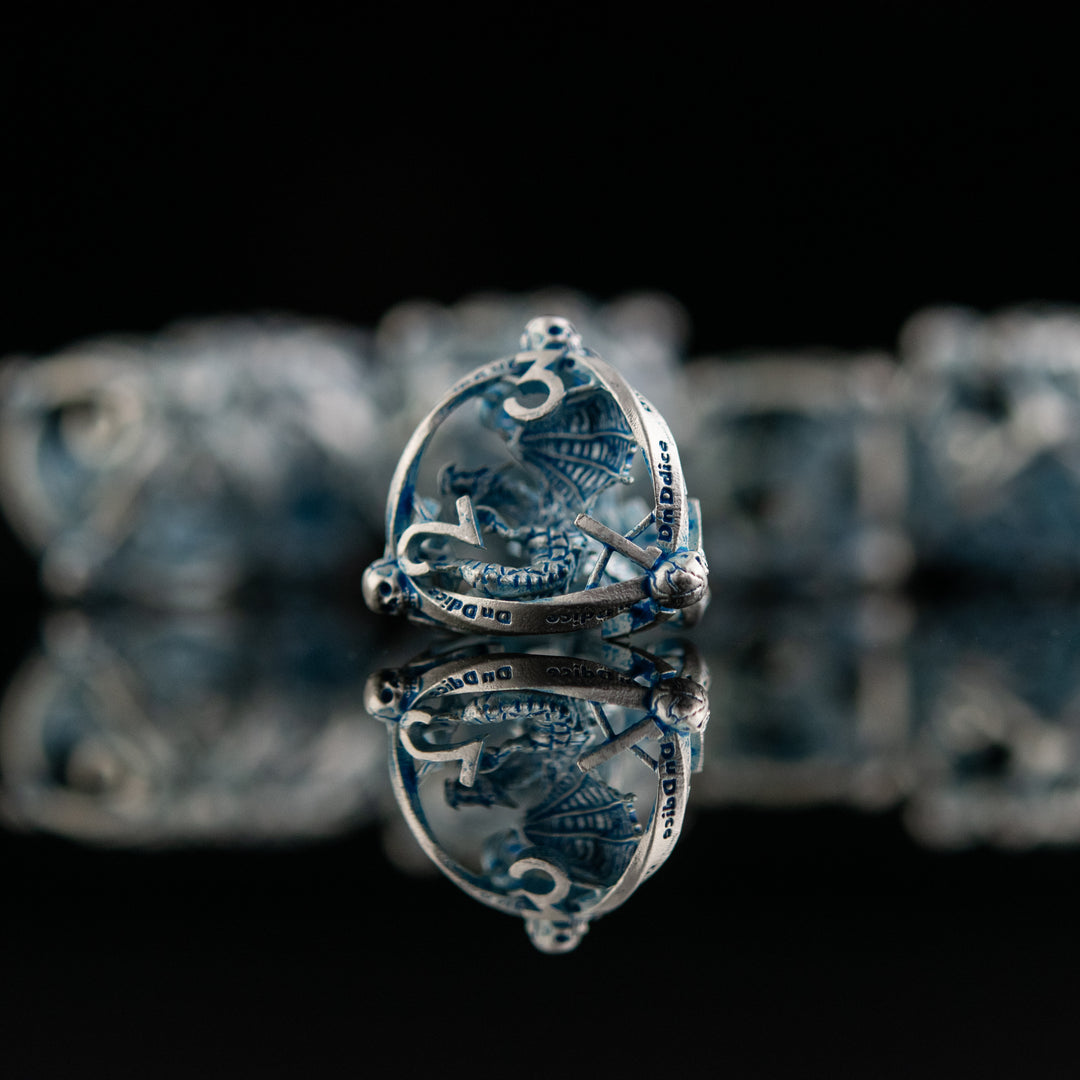 A set of hollow metal dice in silver and blue, displayed on a reflective surface.
