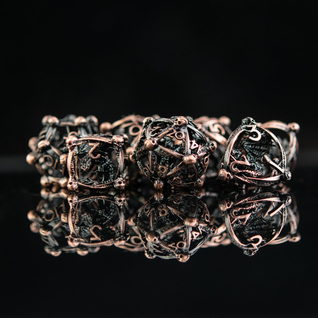 A set of bronze hollow metal dice with embossed numbers and dragons inside, displayed on a reflective surface.