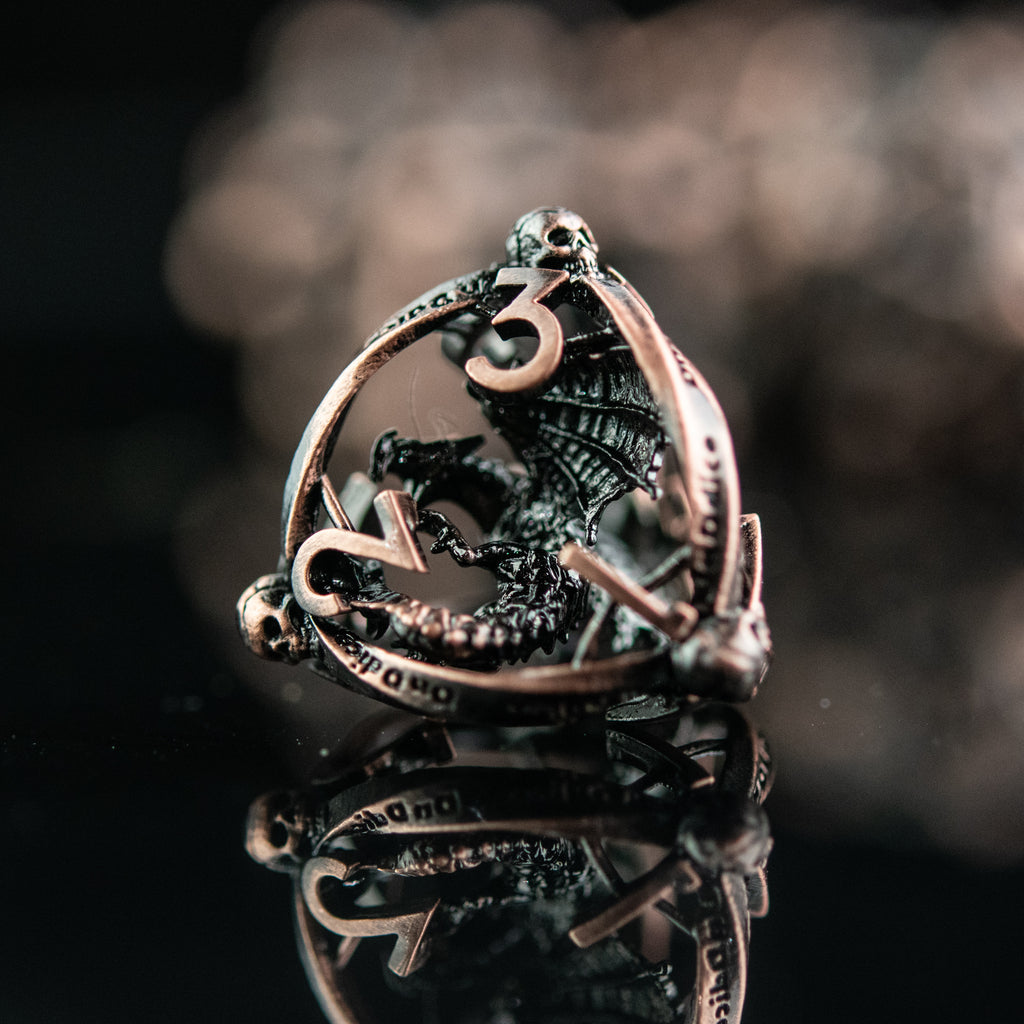 A set of bronze hollow metal dice with embossed numbers and dragons inside, displayed on a reflective surface.