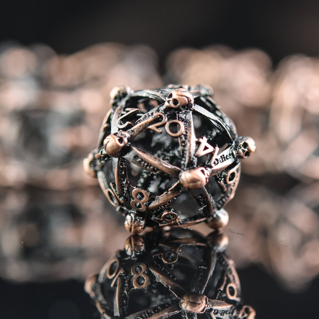 A set of bronze hollow metal dice with embossed numbers and dragons inside, displayed on a reflective surface.