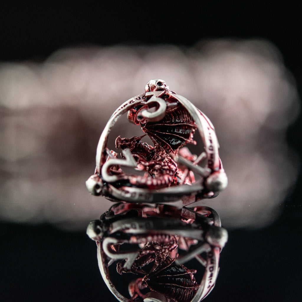 A set of embossed red and silver metal dice with intricate patterns on them, displayed on a reflective surface.