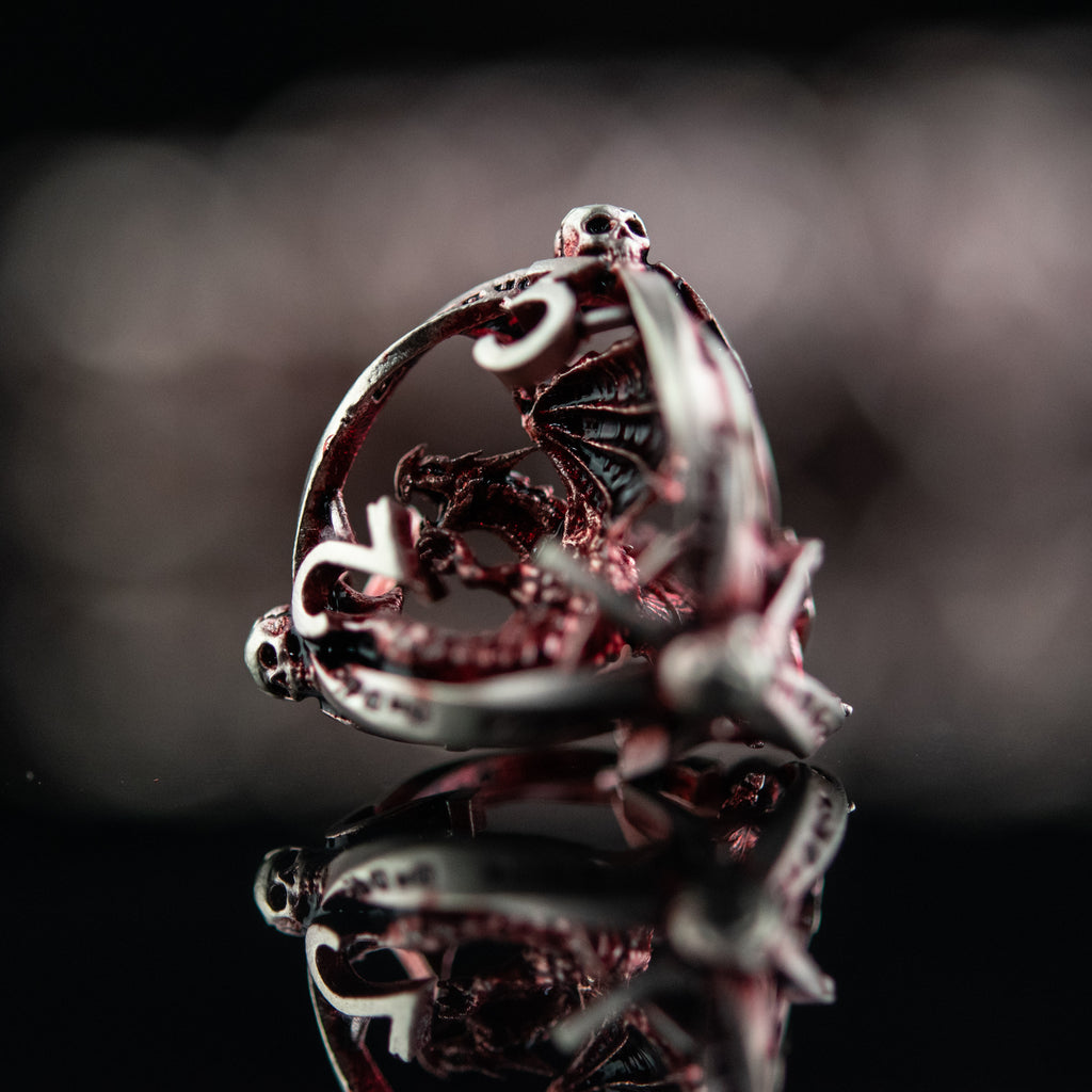 A set of embossed red and silver metal dice with intricate patterns on them, displayed on a reflective surface.