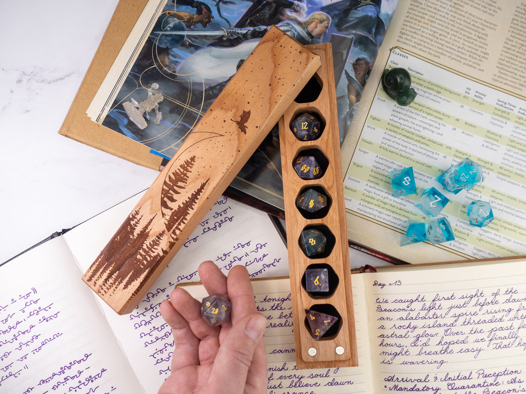 Wooden dice holder with engraved design on a table with books and papers.