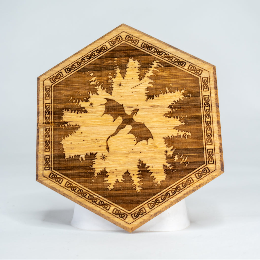 A hexagonal-shaped wooden magnetic art puck with a dragon design amidst trees, intended for customizing Dungeon Master screens.