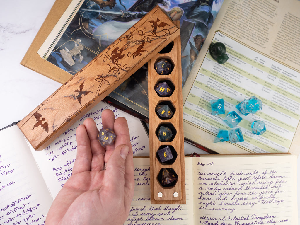Wooden dice tray with engraved designs holding dice, next to a book and papers on a table.