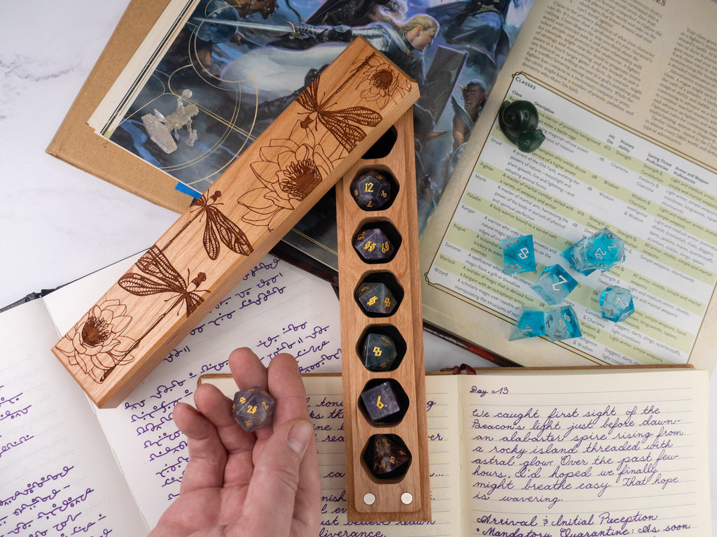 Wooden dice holder with engraved designs on a surface with books and papers.