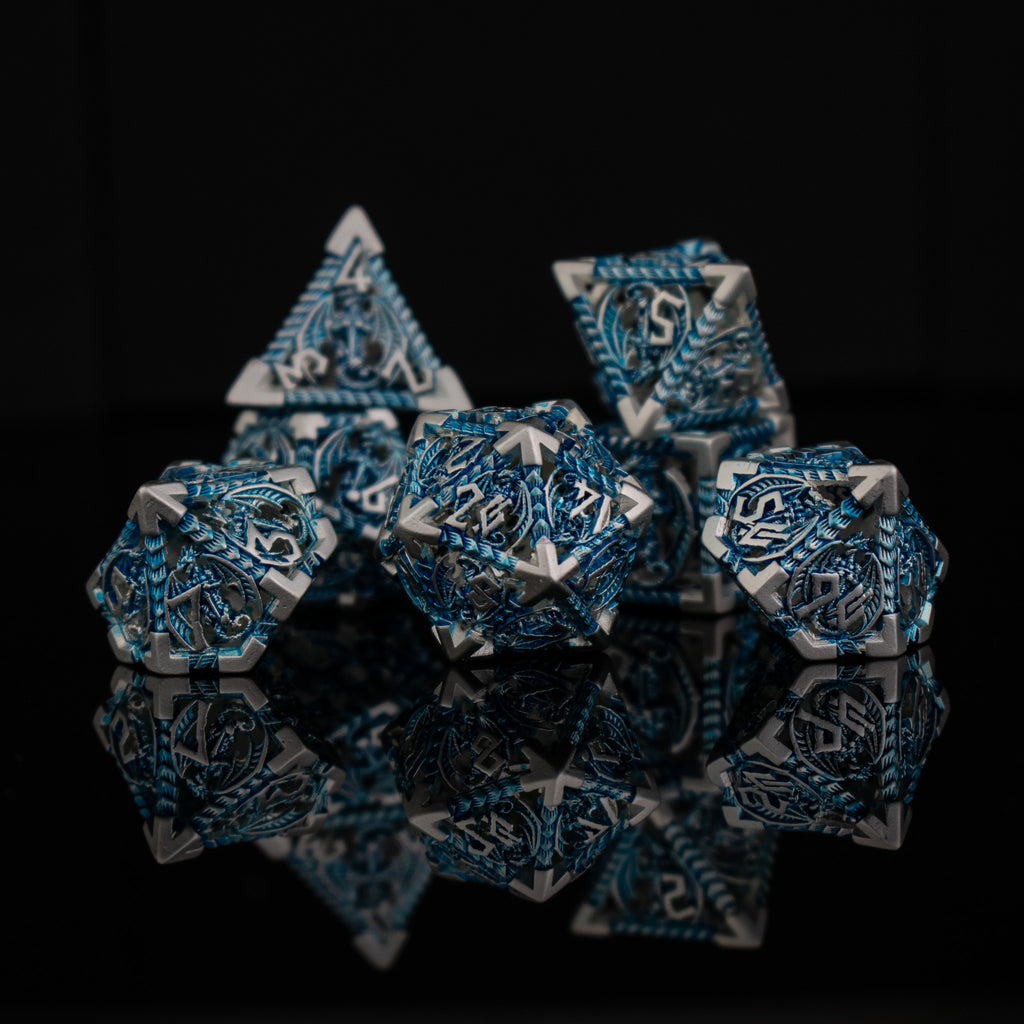 A set of embossed metal hollow dice in silver and blue, with dragons displayed on a reflective surface.