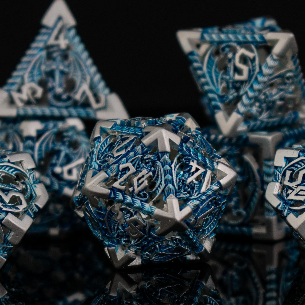 A set of embossed metal hollow dice in silver and blue, with dragons displayed on a reflective surface.