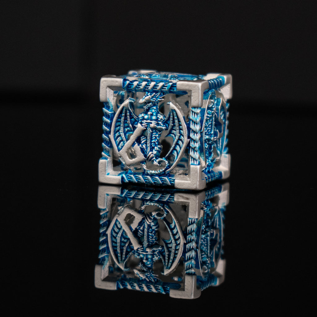 A set of embossed metal hollow dice in silver and blue, with dragons displayed on a reflective surface.