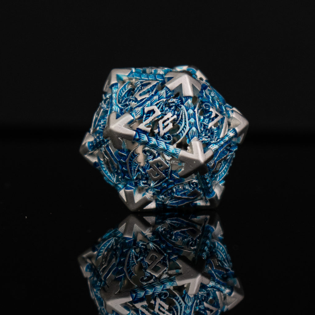 A set of embossed metal hollow dice in silver and blue, with dragons displayed on a reflective surface.