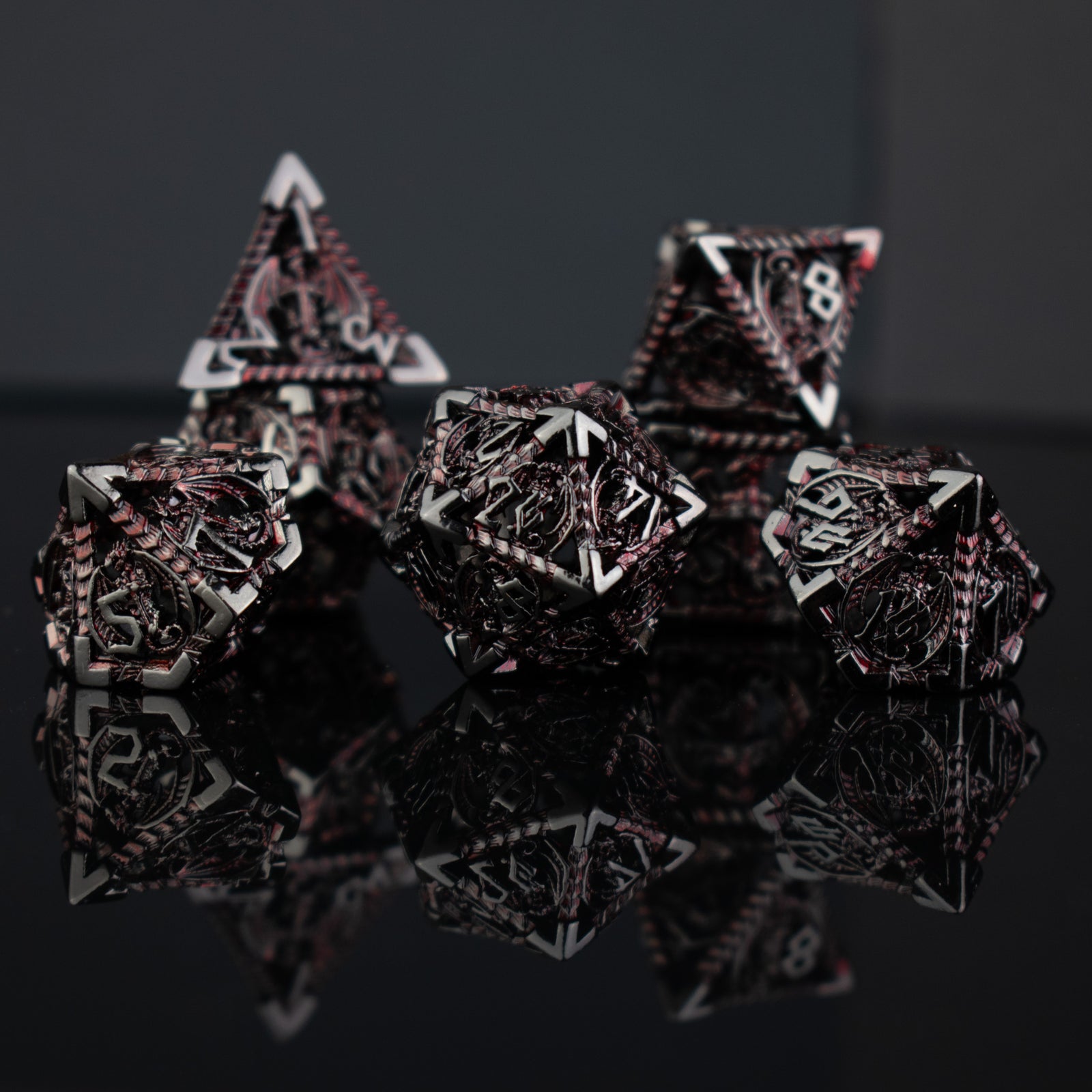 A set of embossed metal hollow dice in crimson and shadow colors, including various shapes such as a d4, d6, d8, d10, d12, and d20, displayed on a reflective surface.