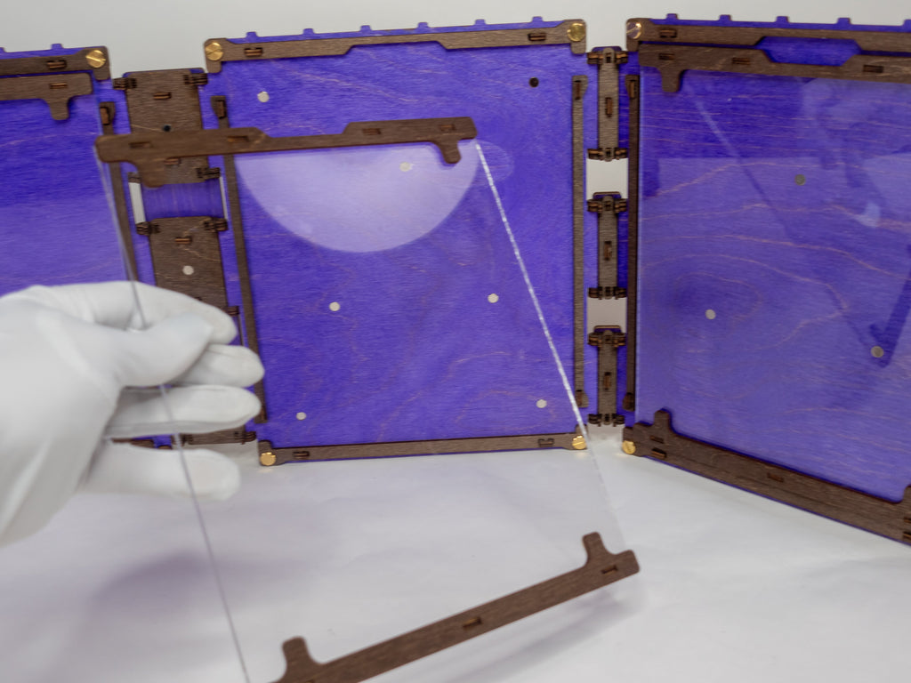 A selection of four compact dungeon master screens in various colors, each featuring a filigree pattern and brass fixtures, with magnetic acrylic panels for displaying maps and notes.