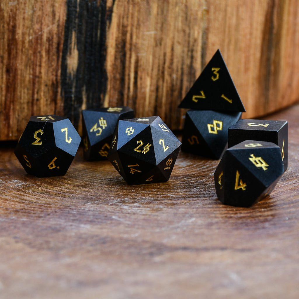 Black polyhedral wood dice with gold numbers on a wooden surface