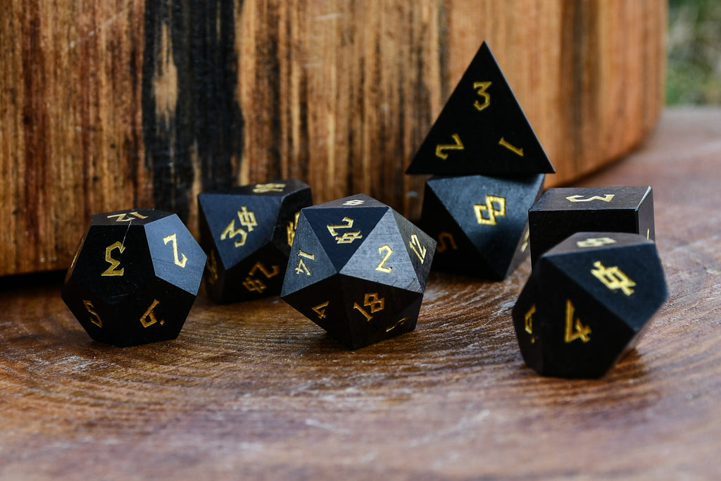 Black polyhedral wood dice with gold numbers on a wooden surface