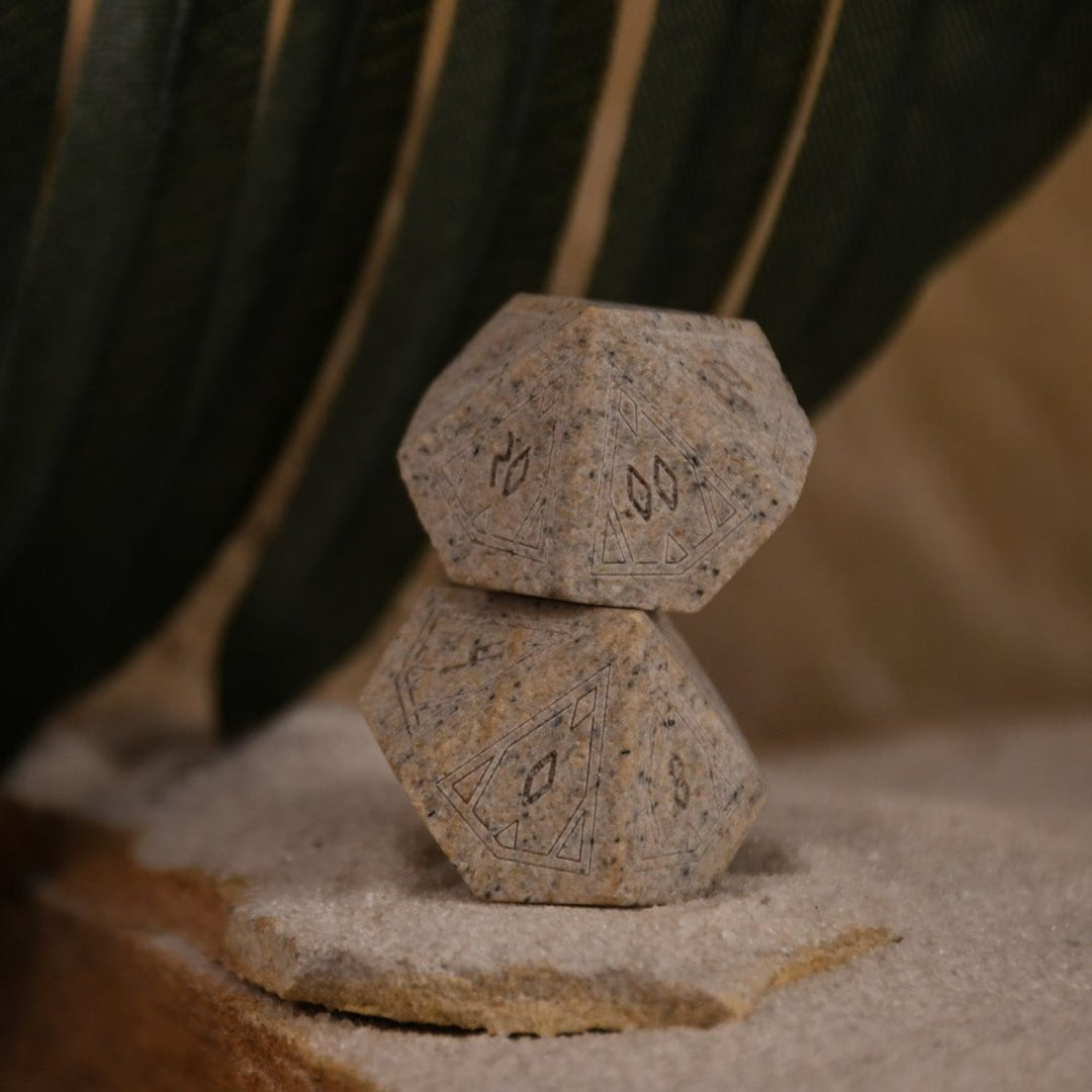 A set Egyptian Limestone Stone dnd dice with engraved numbers and Egyptian-inspired designs, displayed on a sandy surface.