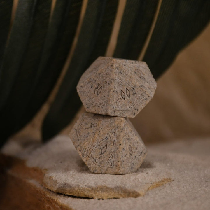 A set Egyptian Limestone Stone dnd dice with engraved numbers and Egyptian-inspired designs, displayed on a sandy surface.