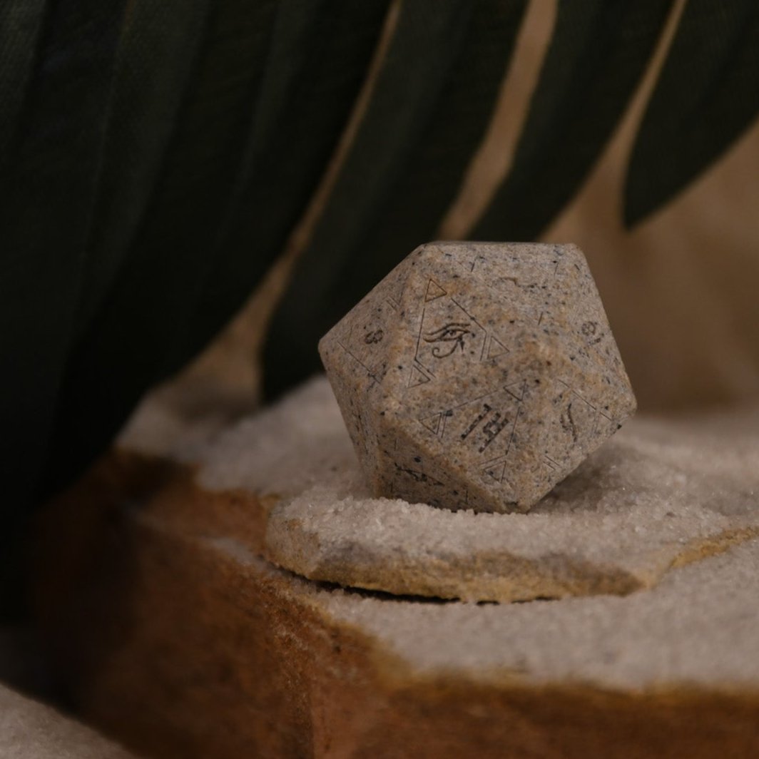 A set Egyptian Limestone Stone dnd dice with engraved numbers and Egyptian-inspired designs, displayed on a sandy surface.