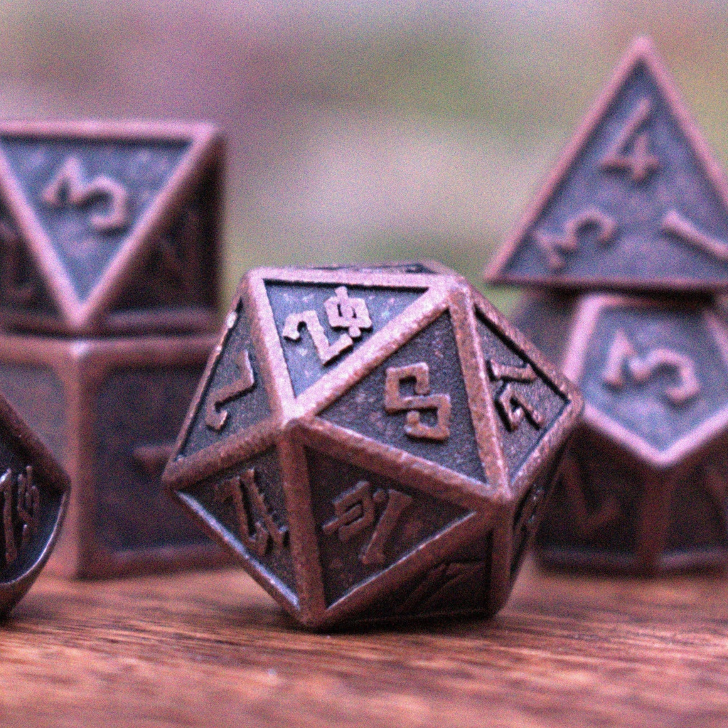 A set of bronze metal dice with embossed numbers, including various shapes such as a d4, d6, d8, d10, d12, and d20, displayed on a wooden surface.