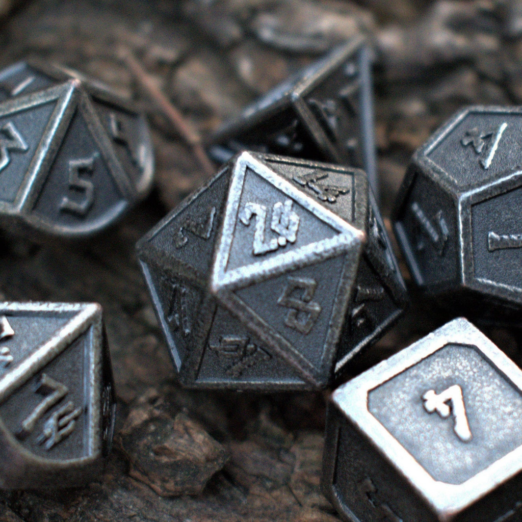 A set of worn silver metal dice with engraved numbers displayed on a wooden surface.