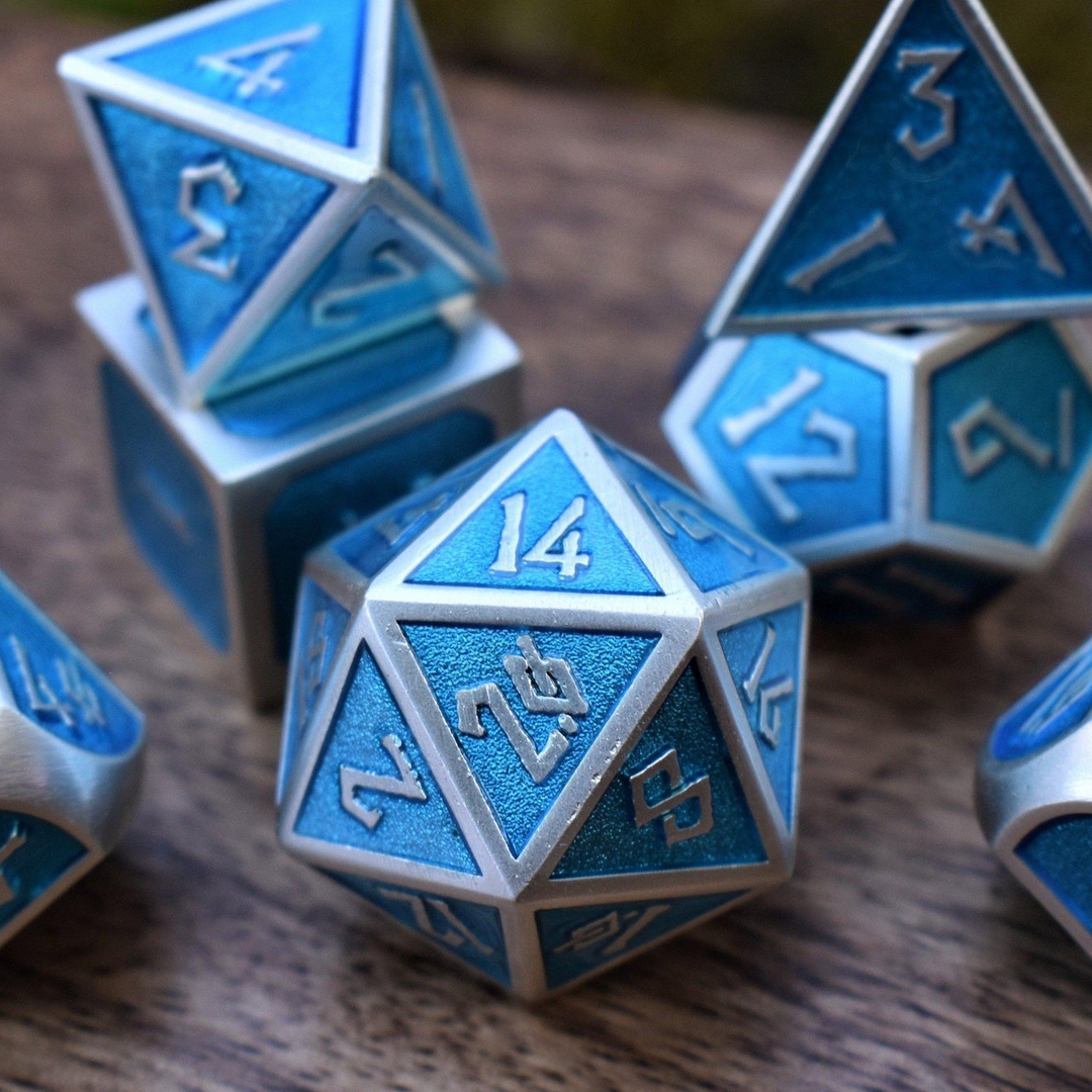 A set of metal dice in blue and silver colors, including various shapes such as a d4, d6, d8, d10, d12, and d20, displayed on a wooden surface.