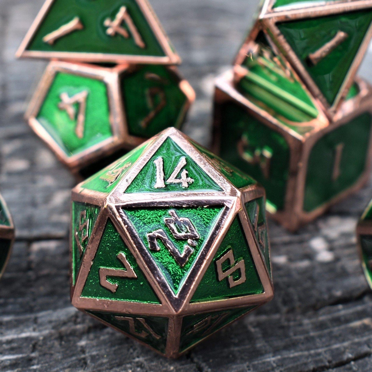 A set of green metal dice with bronze metal edges and embossed numbers, displayed on a wooden surface.