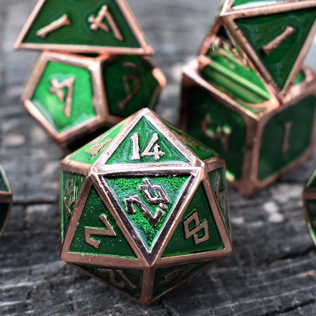 A set of green metal dice with bronze metal edges and embossed numbers, displayed on a wooden surface.