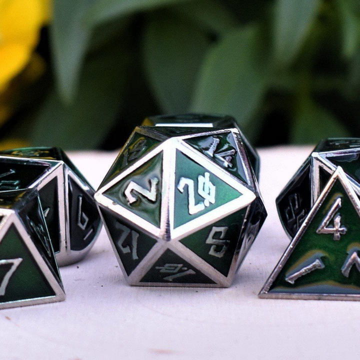 A set of green metal dice with embossed numbers, including various shapes such as a D4, D6, D8, D10, D12, and D20, displayed on a white surface with yellow flowers in the background.