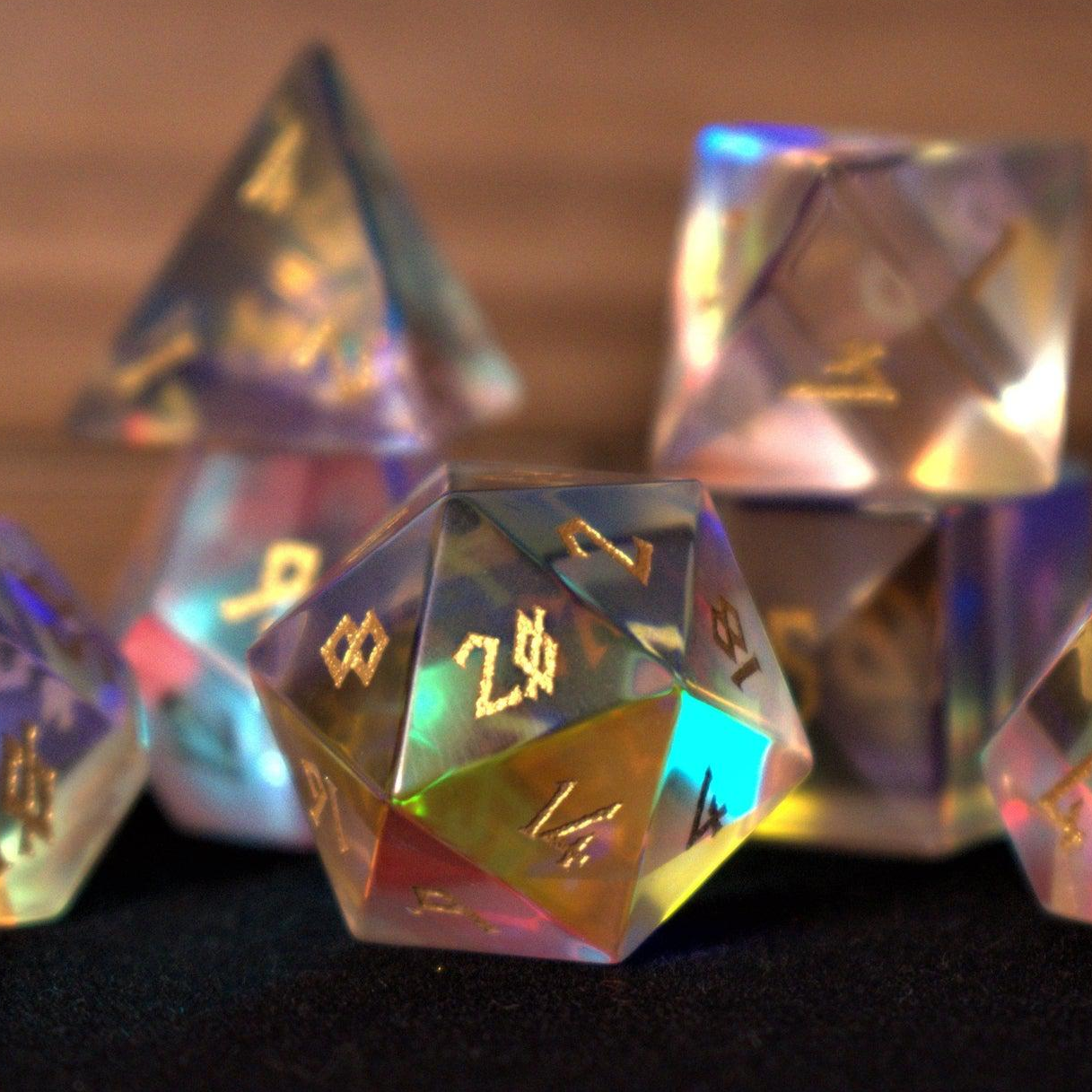 A set of iridescent glass dice with engraved numbers, including various shapes such as a four-sided die (D4), six-sided die (D6), eight-sided die (D8), ten-sided dice (D10), twelve-sided die (D12), and twenty-sided die (D20).