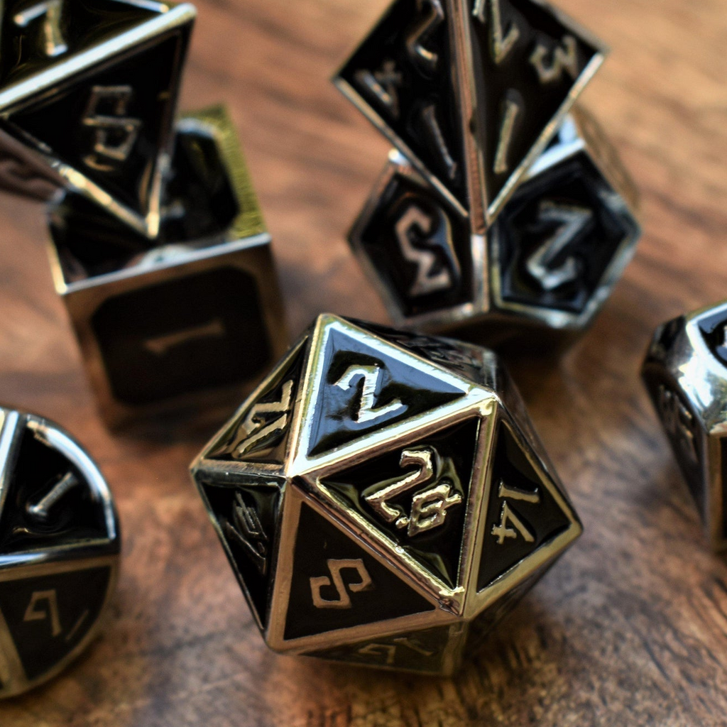 A set of metal dice in silver and black colors, including various shapes such as a d4, d6, d8, d10, d12, and d20, displayed on a wooden surface.