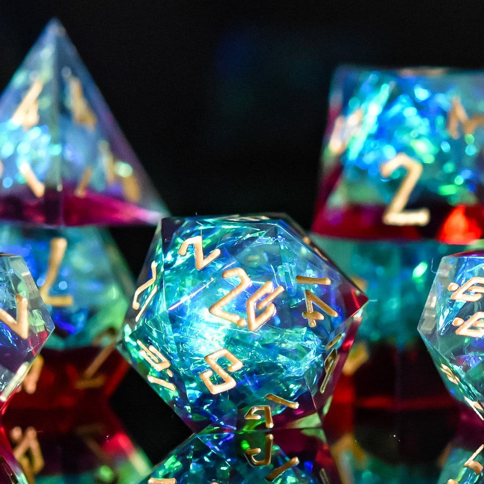 A set of sharp-edged resin dice with engraved numbers, featuring blue, green, and red colors, displayed on a reflective surface.