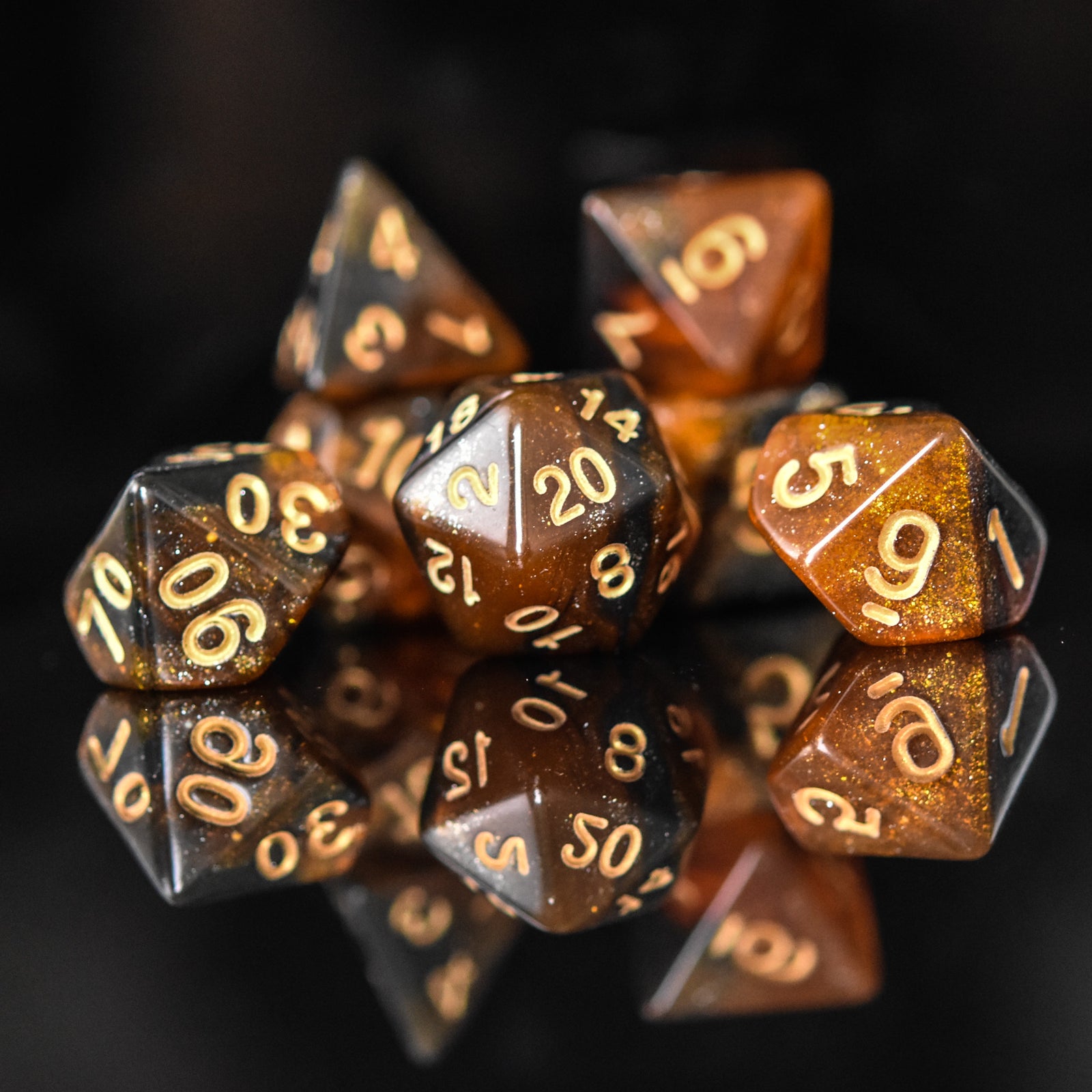 A set of acrylic dice with engraved numbers, featuring a brown color with gold accents, displayed on a reflective surface.